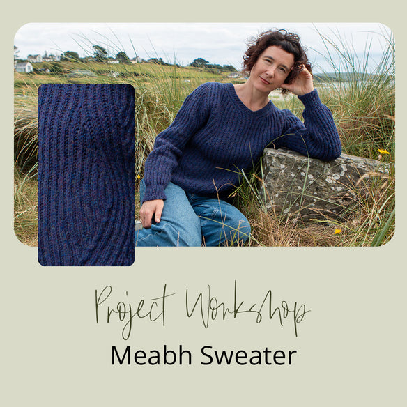 woman leaning on elbow in a blue sweater in grassy field on a stone